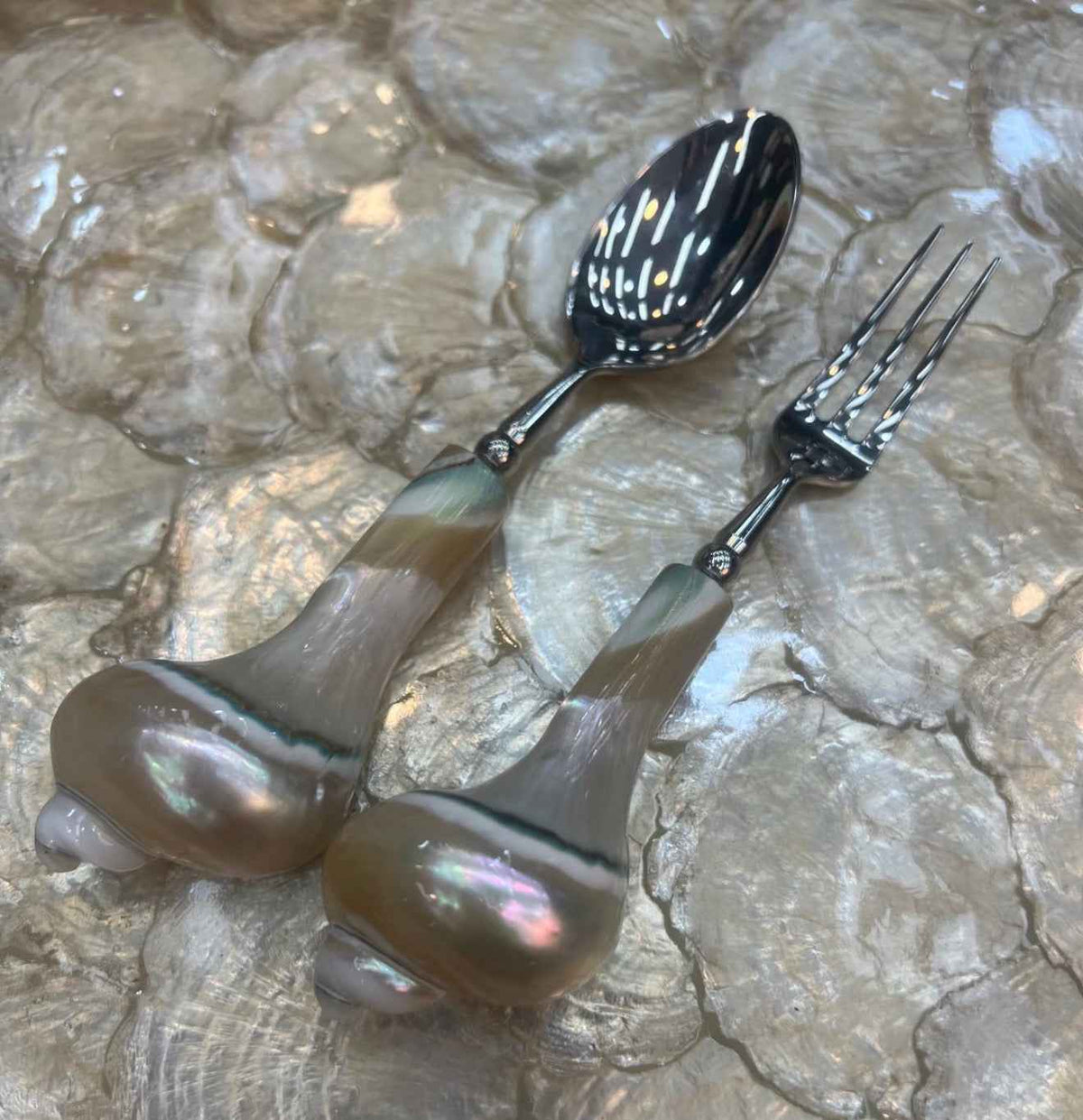 Shell-handled spoon and fruit fork on an iridescent shell surface