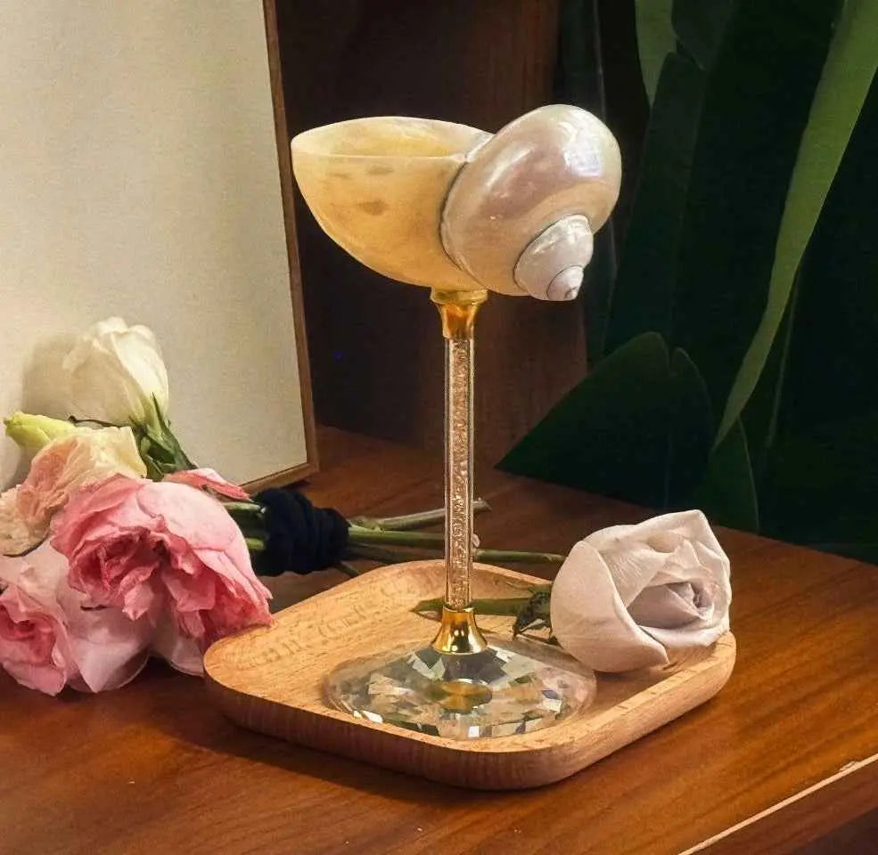 White conch shell goblet styled with flowers on a wooden tray