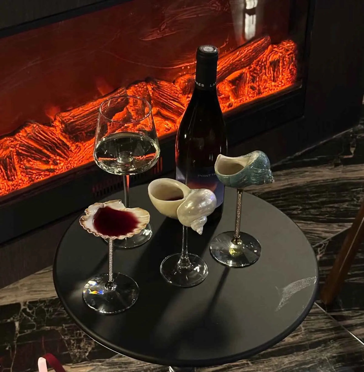 Shell goblets displayed on a table beside a glowing fireplace