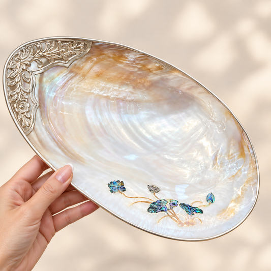 Handheld mother-of-pearl shell tray showing natural iridescence, lotus inlay and floral silver-tone edging