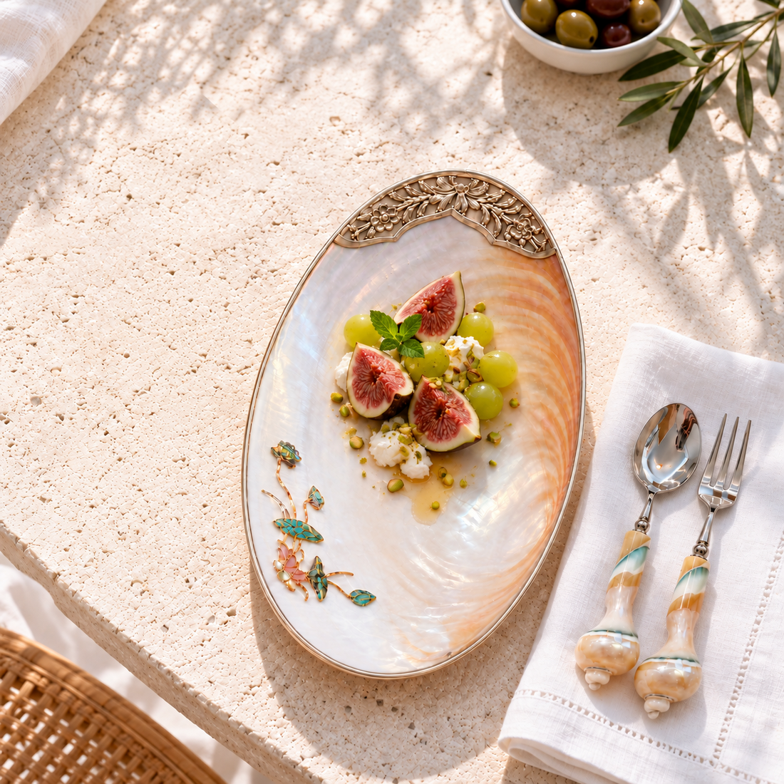 Natural shell platter with fresh figs, grapes, shell-handled cutlery and Mediterranean limestone tabletop