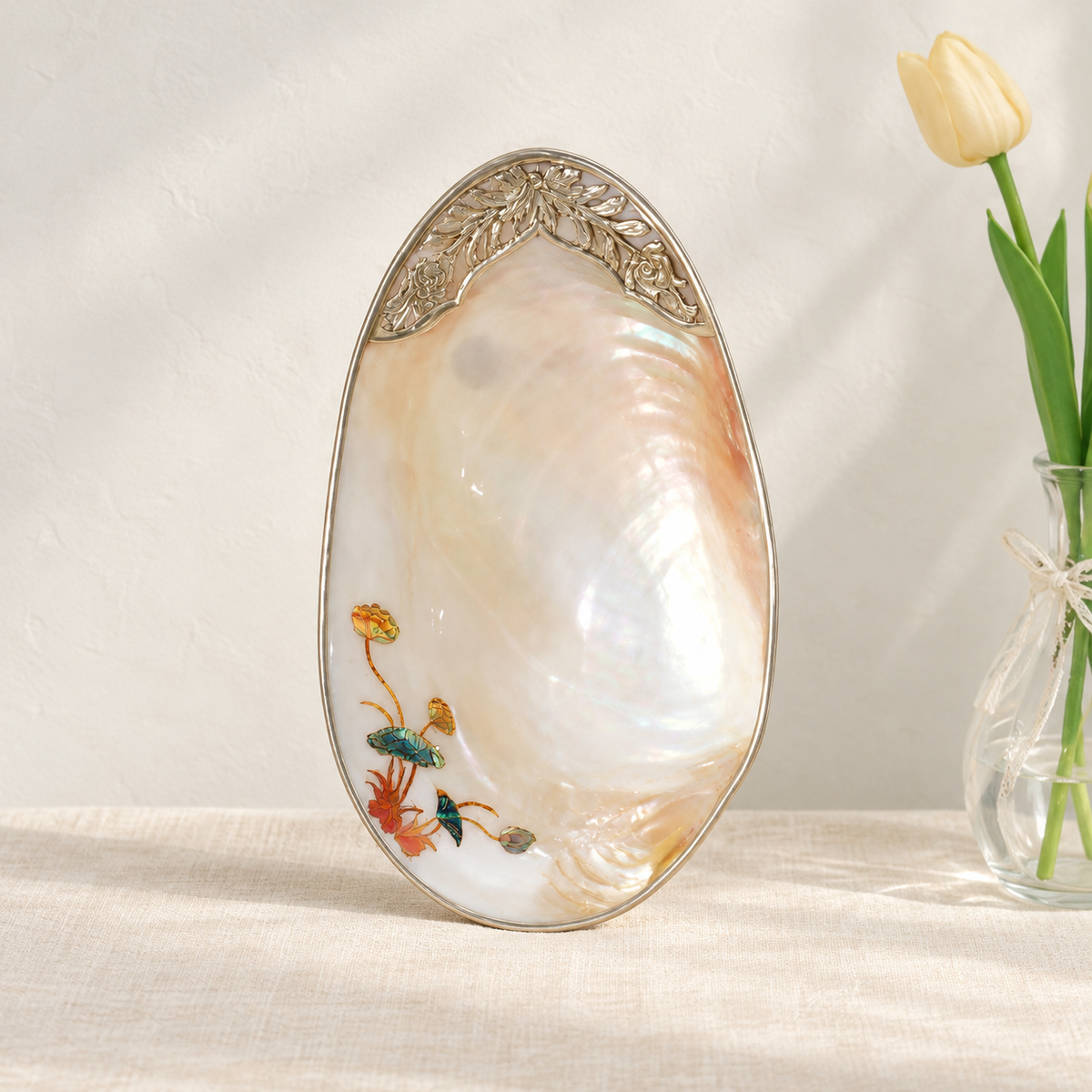 Upright mother-of-pearl shell tray with lotus inlay beside a pale yellow tulip